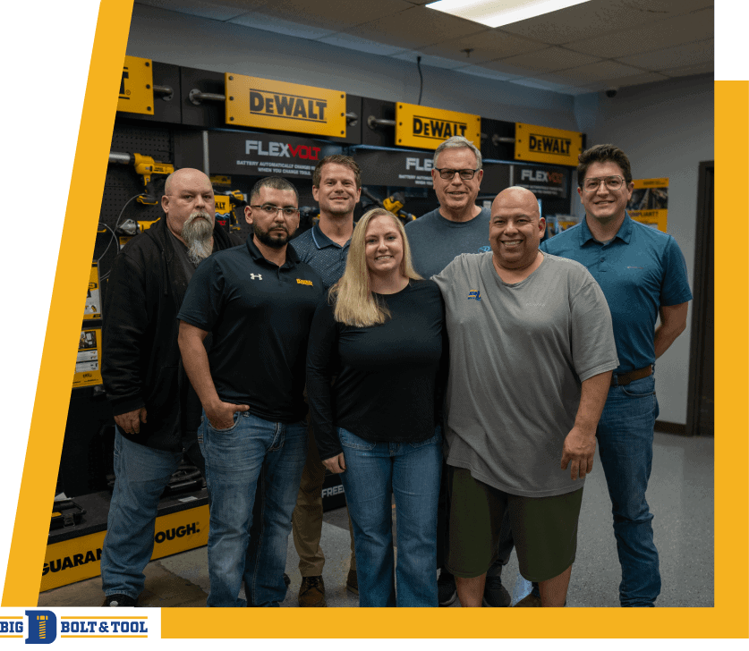 A group of seven people standing together in front of shelves with DeWalt tools.