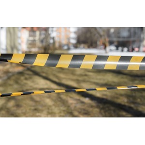 close up of yellow and black caution tape blocking off an outdoor area with blurred buildings and trees in the background.